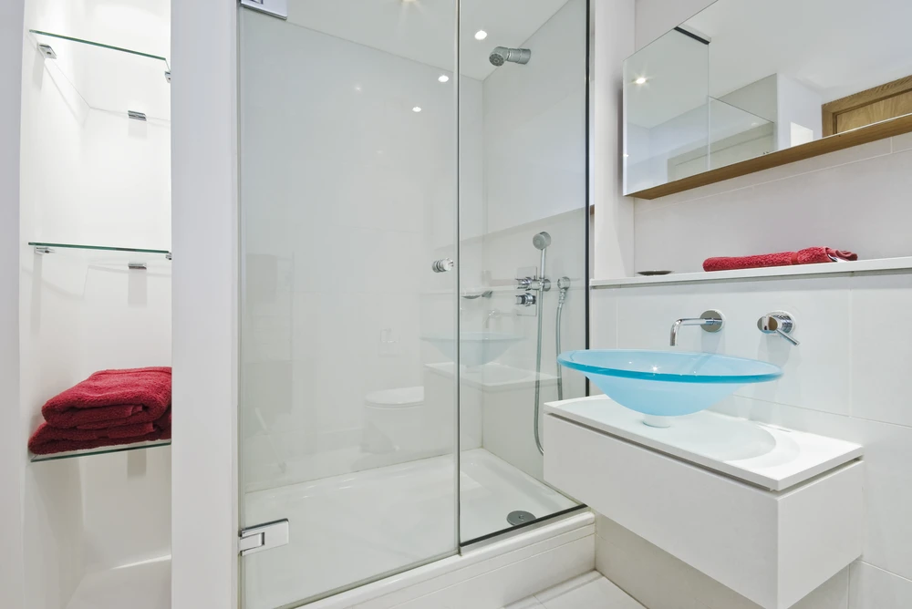 Salle de bain moderne avec douche à l'italienne vitrée, vasque en verre bleu translucide posée sur meuble suspendu blanc