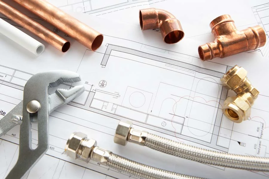Outils et matériaux de plomberie disposés sur plans techniques d'installation