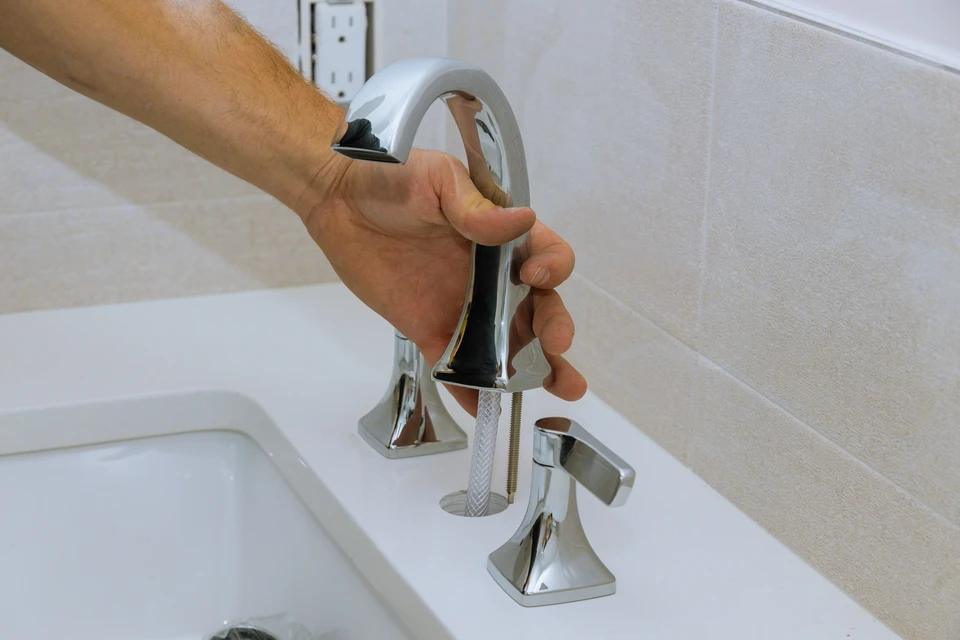 Main d'un plombier tenant et manipulant un robinet de baignoire chromé dans une salle de bains moderne