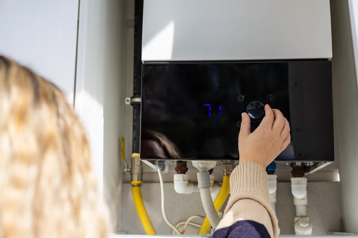 Un plombier en polo blanc travaille accroupi dans un local technique, intervenant sur un système de chauffage